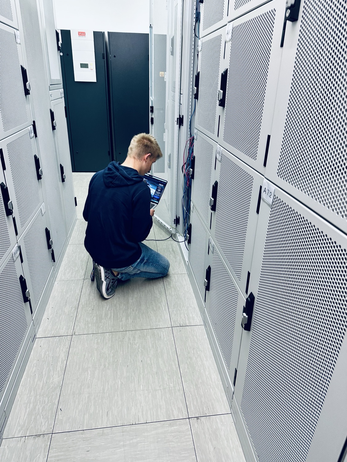 Ein Techniker von NETFACTORY kniet mit Laptop zwischen den Serverschränken im Rechenzentrum